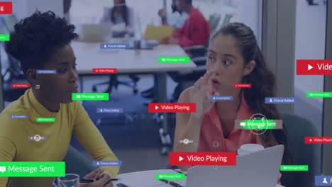 Animación-De-Textos-E-íconos-En-Cuadros-De-Mensajes,-Diversas-Compañeras-De-Trabajo-Discutiendo-Informes-En-Una-Computadora-Portátil