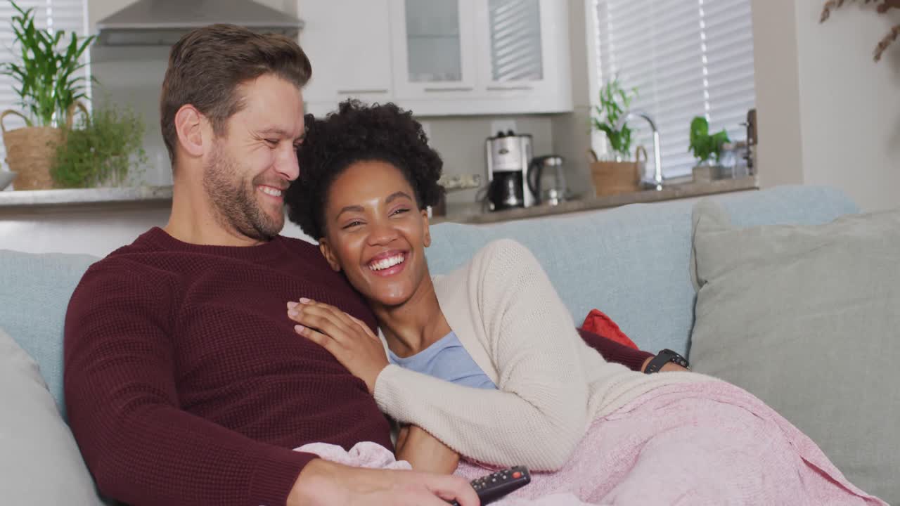 Video of happy diverse couple watching tv on sofa