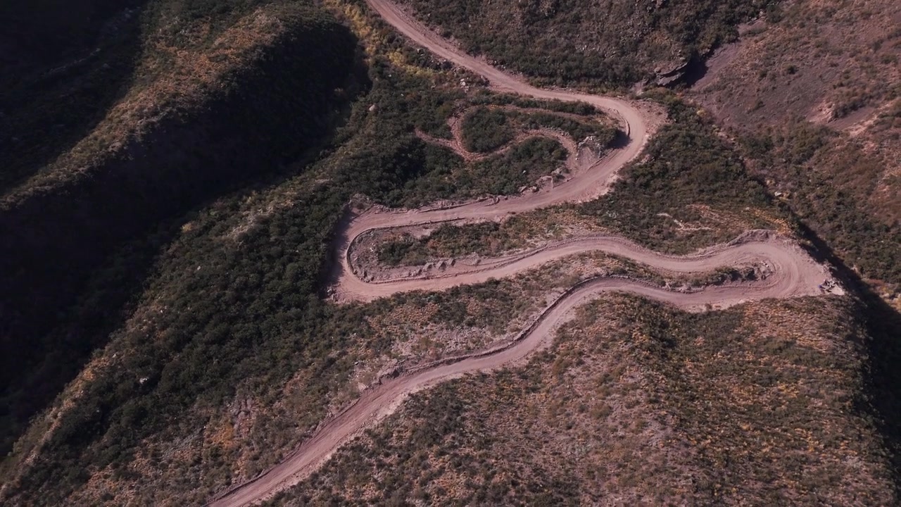 Ripresa aerea con drone che svela la cima di una collina tra montagne erbose con una strada in Argentina.