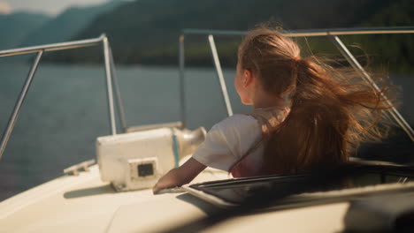 smiling little girl with spine brace sits on motorboat deck at windy seaside. positive child sails yacht in ocean on exotic vacation. family water trip