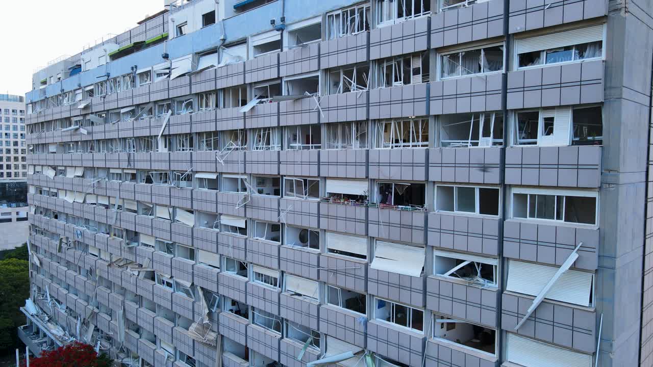 Drone lowers along a building in Tel Aviv with broken windows and visible interior damage.