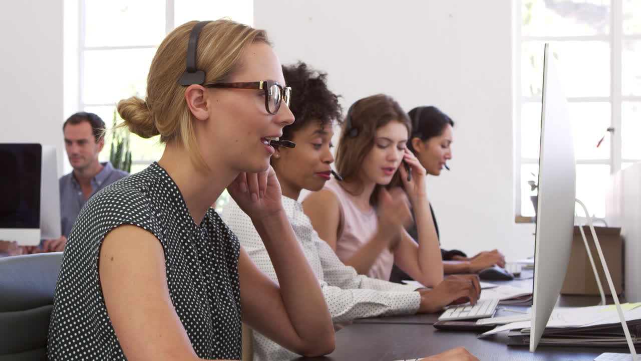 una fila de mujeres usando auriculares de teléfono en una oficina de plan abierto