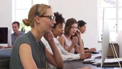 a row of women using phone headsets in an open plan office