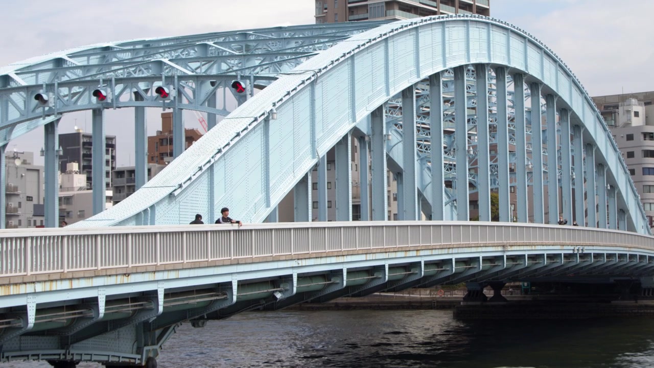 Panning Shot of a Blue Arch Bridge and City Buildings by the River