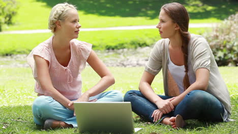 un par de chicas miran una computadora portátil y luego hablan entre sí