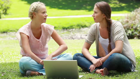 a pair of girls look at a laptop and then talk to one another