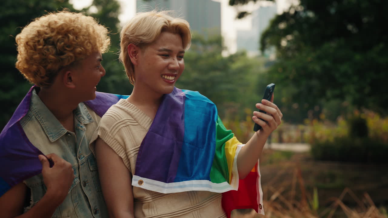 Two friends taking a selfie with pride flags in the park