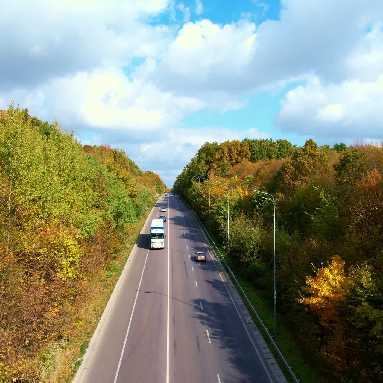 High speed road going through the beautiful forest on early autumn season. Drone footage over the motorway with riding cars on sunny day