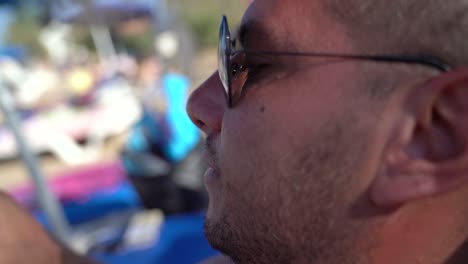 Close-up-of-a-man-relaxing-on-the-beach-as-he-answers-his-phone