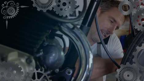 Animation-of-turning-cogs-over-caucasian-male-mechanic-fixing-motorcycle-and-talking-on-smartphone