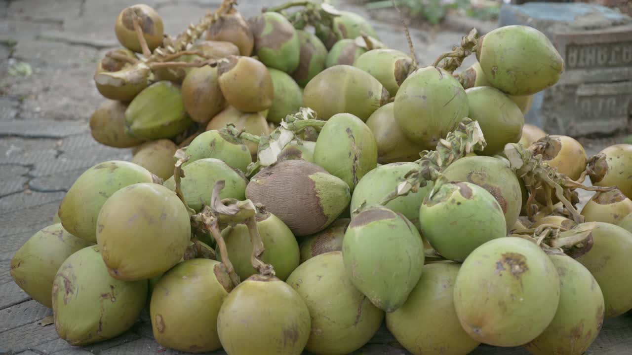A large pile of fresh green tender coconuts sits on a paved street in India, ready for sale during the hot summer season. Perfect for travel and food documentaries
