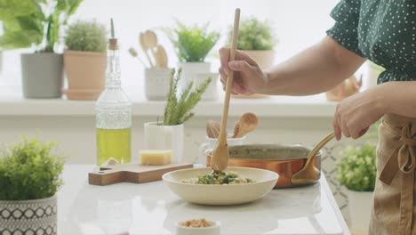 mujer de la cosecha poniendo pasta en el plato en la cocina