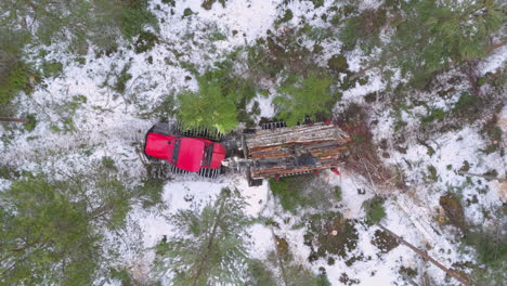 forwarder with grapple loader transports felled logs in snowy forest, top drone