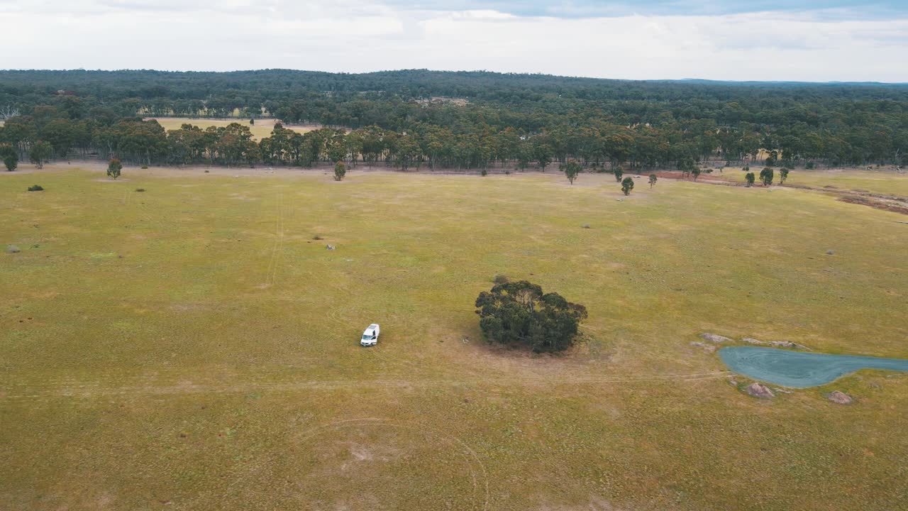 Drone aerial over an empty Australian field with a campervan in the middle