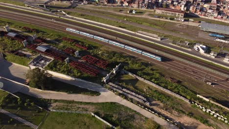 Vista-Aérea-De-Arriba-Hacia-Abajo-Del-Tren-De-Cercanías-Que-Circula-Por-La-Vía-Y-Se-Acerca-Al-Complejo-Ferroviario