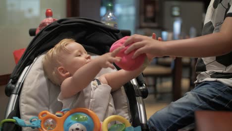 Ein-Kleines-Mädchen,-Das-In-Einem-Kinderwagen-Sitzt-Und-Mit-Seinem-älteren-Bruder-Spielt