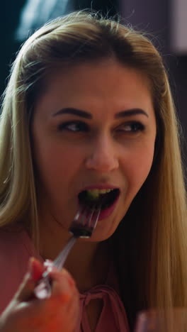 happy blonde young woman eats tasty salad and enjoys conversation with sweetheart at table during romantic dinner at home closeup slow motion