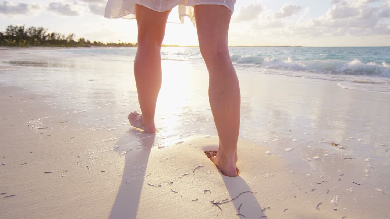 Gambe di donna caucasica a piedi nudi sulla spiaggia oceanica
