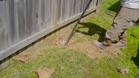 man using a prybar to dig out a post hole