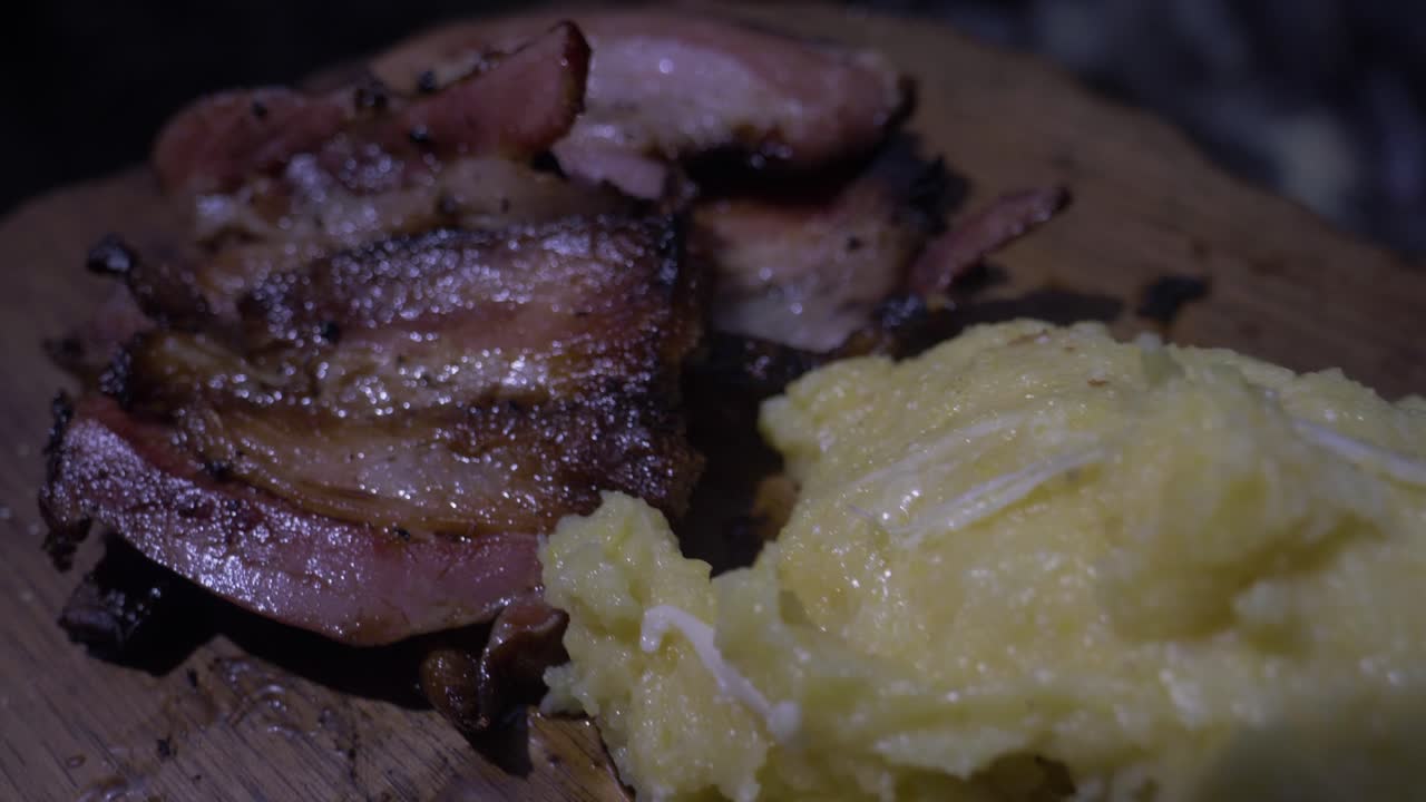 Ham with grilled polenta over low heat, presented on a wood chopper. The ham is well browned. The polenta is made with cheese that melts over it