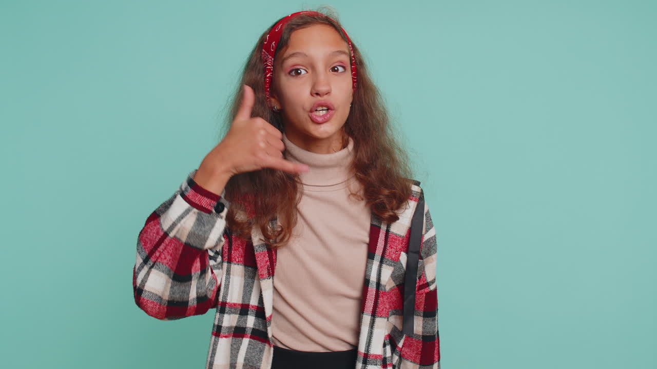 niña niño mirando a la cámara haciendo gesto de teléfono como dice hola me llamas, número de contacto