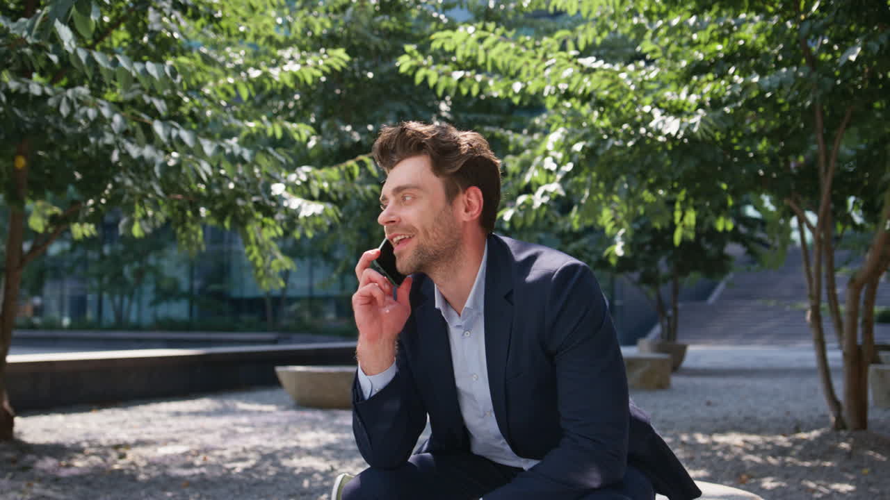 웃는 매니저가 공원에서 휴대전화로 전화를 하고 있다.