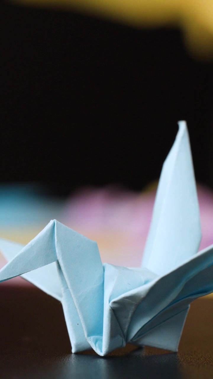 A light blue origami crane sits on a dark surface under soft studio lighting