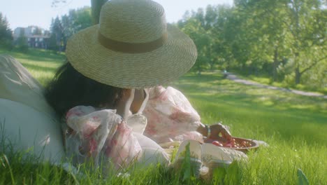 Schwarze-Frau-Mit-Sonnenhut,-Die-Auf-Der-Seite-Liegt,-Auf-Einem-Picknick-Im-Park,-Das-Trauben-Isst