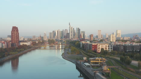 Frankfurt-am-Main,-Germany-Skyscraper-Skyline-View-slow-Dolly-out-revealing-Bridge-over-Main-River-at-Sunrise,-Aerial-backwards