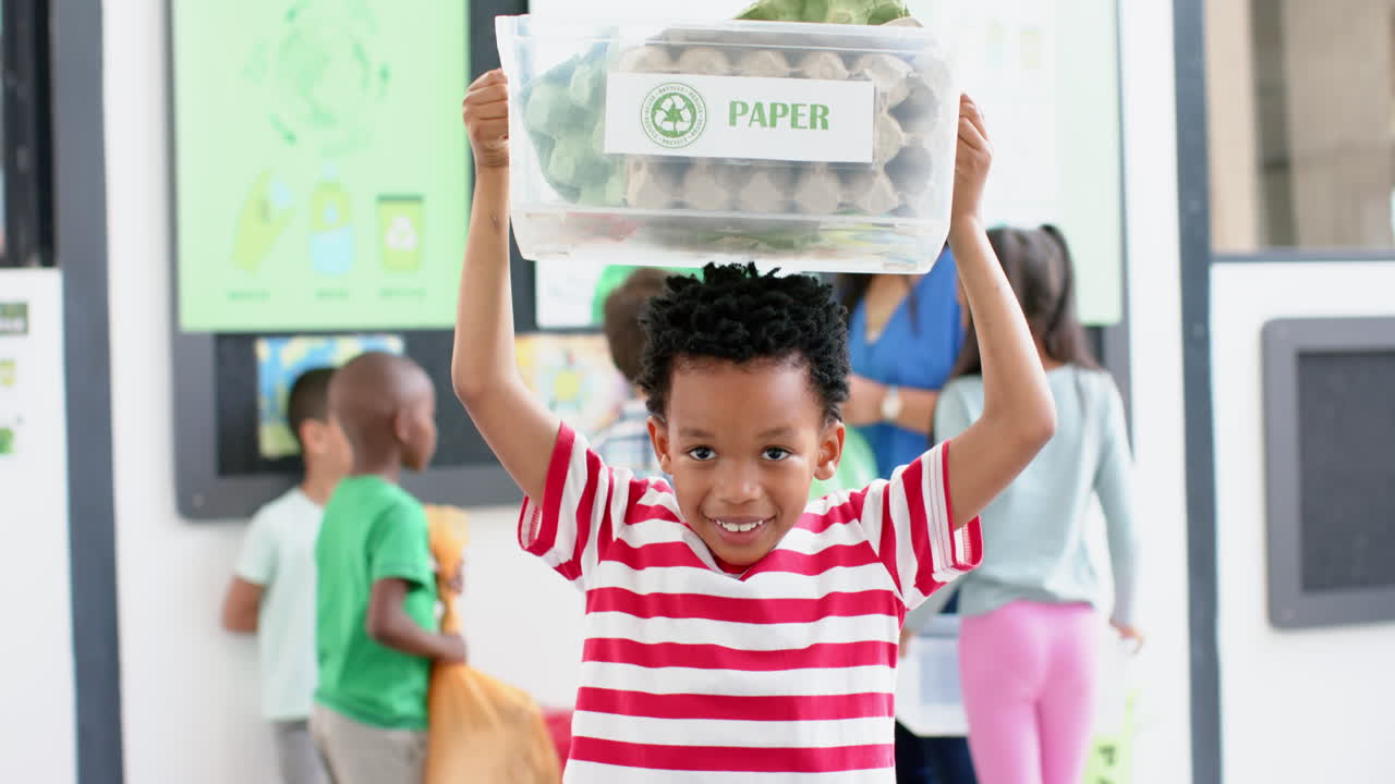 In school, boy holding recycling bin labeled Paper during recycling activity