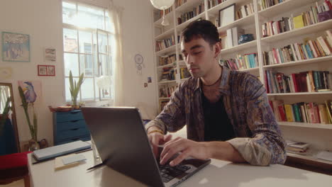 young man opening laptop and typing in cozy sunlit room