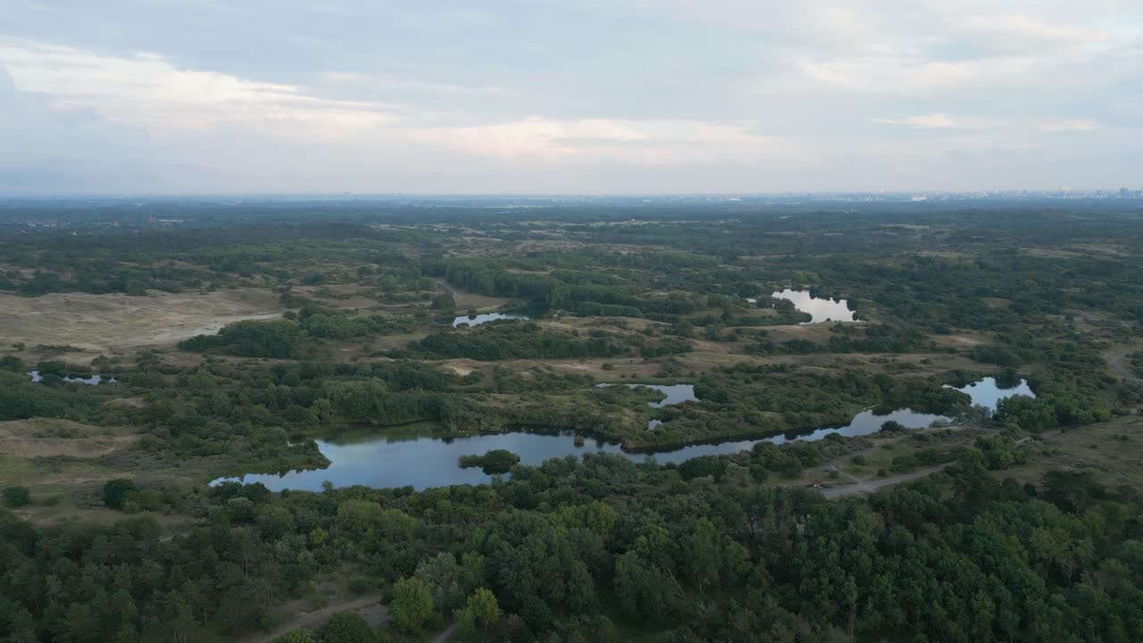 Stunning drone footage over the Wassenaarse Slag showing interconnected lakes and green dune valleys under a soft evening sky