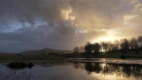 La-Puesta-De-Sol-Se-Encuentra-Con-Nubes-Oscuras-Reflejadas-En-El-Lago-Con-árboles