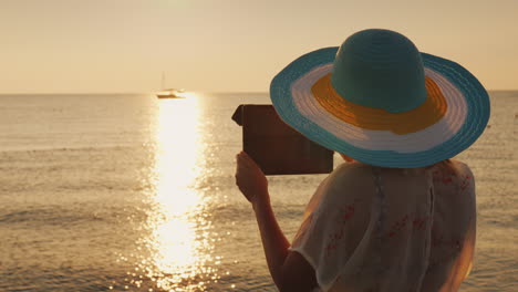 una mujer con un sombrero está tomando fotos de un hermoso amanecer en el mar 4k video