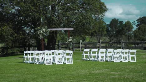 Reihen-Von-Gaststühlen,-Die-Während-Einer-Hochzeit-Im-Freien-Auf-Einer-Wiese-Mit-üppigen-Bäumen-Im-Hintergrund-Angeordnet-Sind