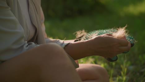 close-up hand removing collected dog fur from grooming glove with warm sunlight highlighting fur strands, showcasing fur removal details, blurred greenery in background provides natural ambiance