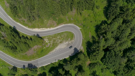 Drone-Shot-of-an-Alpine-Road-in-a-Forest-with-Cars-driving-by,-Tilting-down