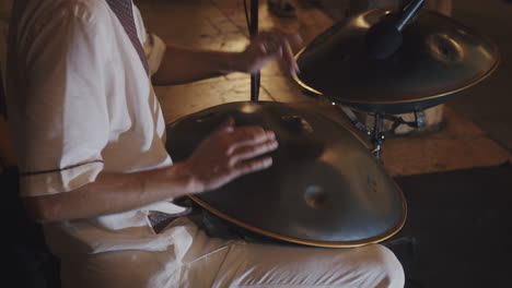 busker artist in white robe plays handpan on the street during summer festival