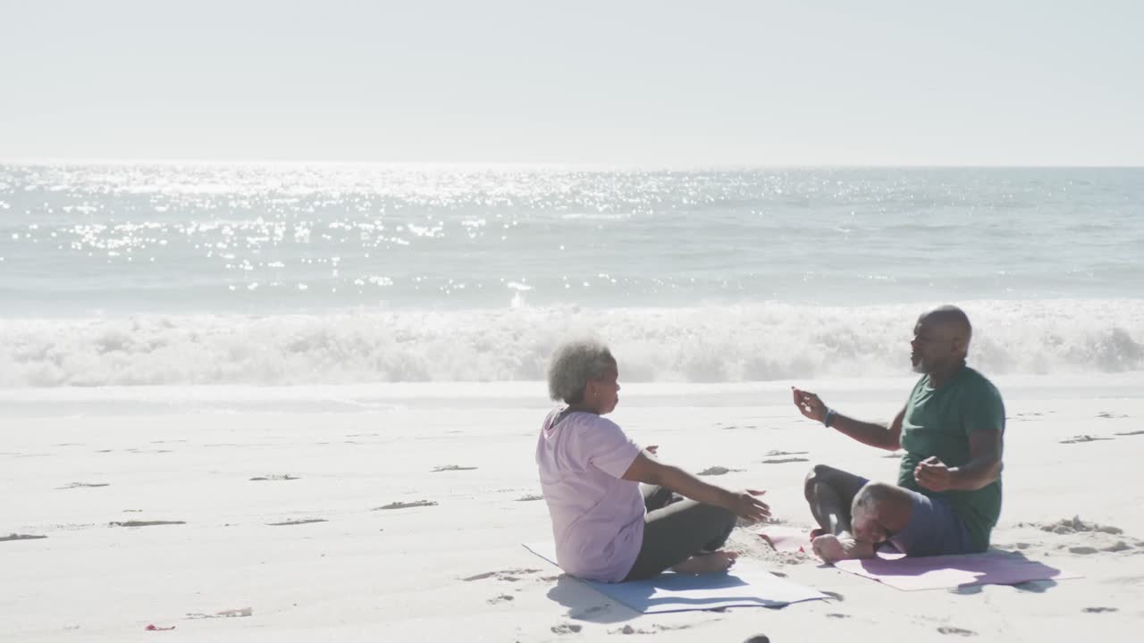 해변에서 요가와 명상을 하는 행복한 아프리카계 미국인 커플, 스로우 모션으로 복사 공간