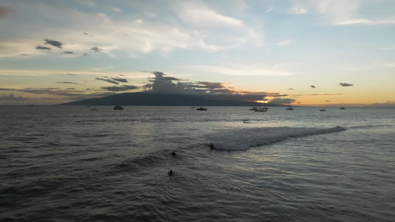 밤 보디보더들은 라하이나 마우이에서 보트 뒤에서 해가 질 때 마지막 파도를 즐깁니다.