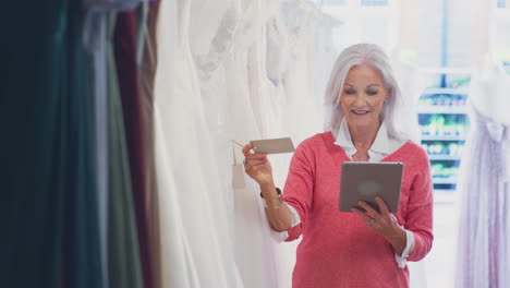 senior female owner of bridal wedding dress shop with digital tablet