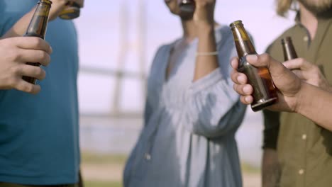 closeup shot of friends clinking beer bottles and dancing