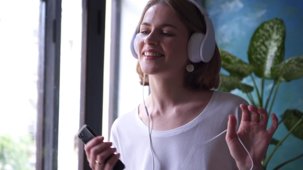 joven escuchando música y cantando cerca de la ventana