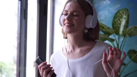 young woman listening to music and singing near window