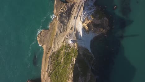 Directamente-Sobre-El-Faro-De-Castlepoint-En-Nueva-Zelanda,-Moviéndose-A-Lo-Largo-De-La-Cresta-De-Un-Acantilado-Hacia-Una-Bahía-Rocosa-Y-Una-Playa