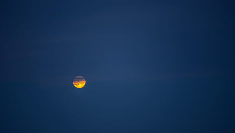 Low-angle-shot-of-full-moon-rising-in-the-night-sky-over-dark-clouds-in-timelapse