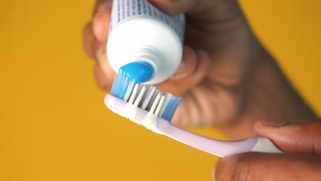 close-up of a hand squeezing toothpaste onto a toothbrush