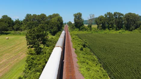 a drone shot following a train from above as it travels through farm fields. a bright sunny sky is above and the midwest landscape is rushing by