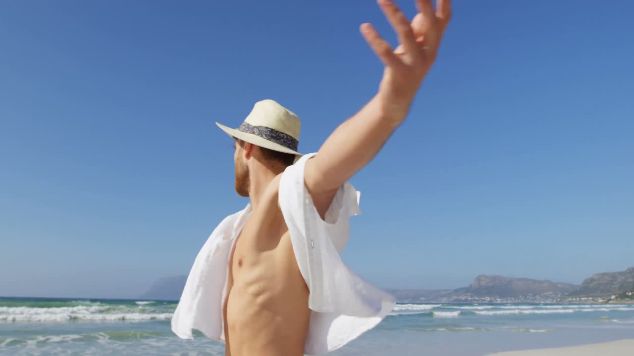 해변 4k에 팔을 펴고 서 있는 모자를 입은 남자