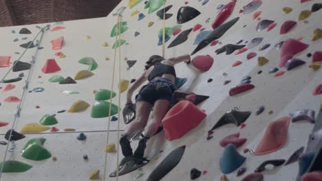 mujer joven practicando escalada en roca en una pared de roca en el interior